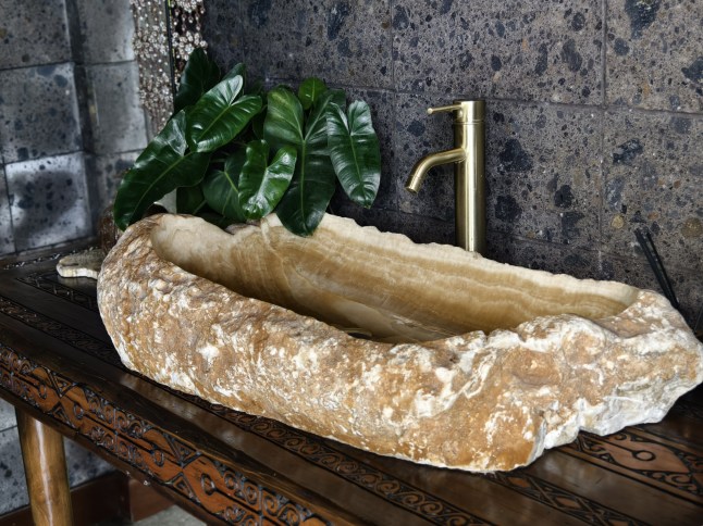 A uniquely crafted sink made from a large natural stone basin, with a modern brass faucet and tropical leaf decor; Shutterstock ID 2638252071; purchase_order: -; job: -; client: -; other: