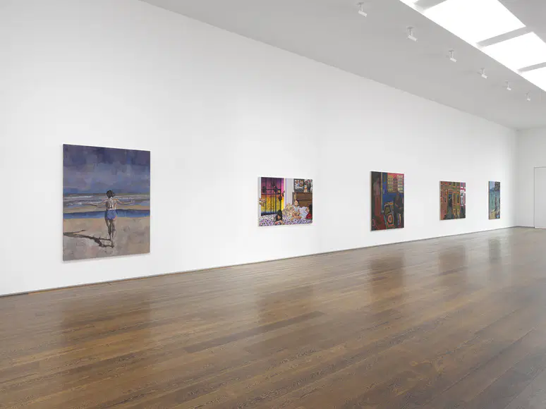 Contemporary art gallery interior with various paintings displayed on a white wall and wooden flooring.