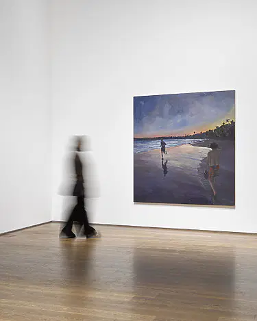 Person walking past a large painting in an art gallery, featuring a coastal scene with two figures at sunset.