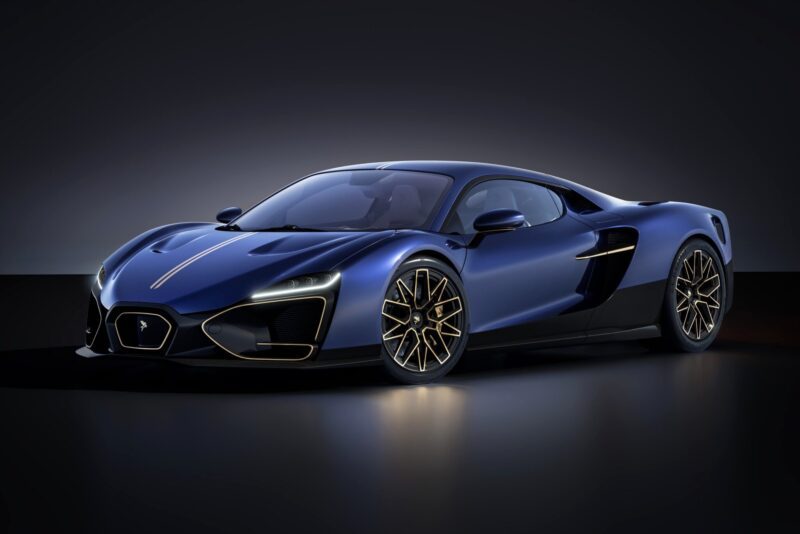 A sleek, blue sports car with gold accents and aerodynamic design is parked on a dark, reflective surface—one of the 20 Cars That Focused on Analog engagement in 2025—against a black background.