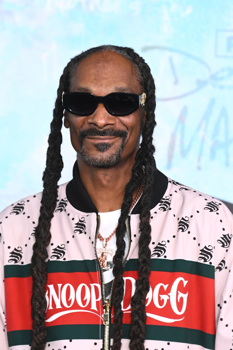 Person with sunglasses and braided hair wearing a stylish patterned jacket with the text "Snoop Dogg" on the front