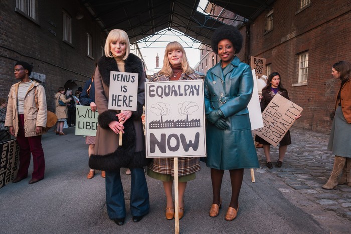Helen George as Trixie Franklin, Natalie Quarry as Rosalind Clifford and Renee Bailey as Joyce Highland in Call the Midwife Helen George as Trixie Franklin, Natalie Quarry as Rosalind Clifford and Renee Bailey as Joyce Highland, holding signs saying VENUS IS HERE and EQUAL PAY NOW.