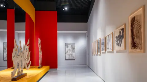 Qatar Foundation A gallery with a red panel on the left is seen dotted with paintings made by MF Husain at the  Lawh Wa Qalam museum