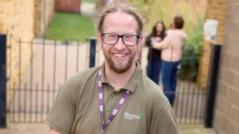 Moulton College A man with light brown hair and glasses smiles at the camera.