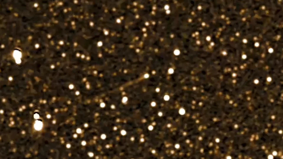 A streak of white light is seen amidst a starry golden deep space image.