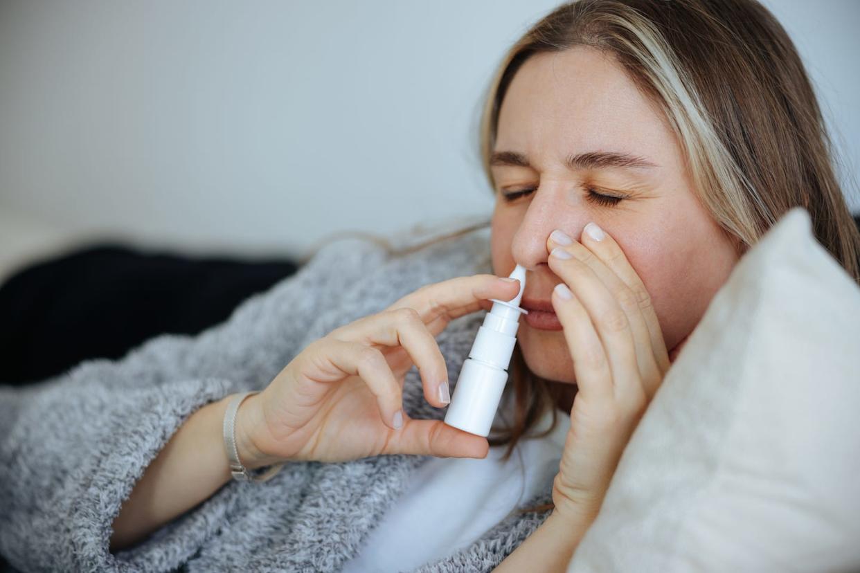 sick young woman using nasal spray