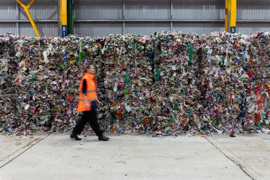 Piles of recycled soft plastic at the SPEC facility near Taree, with a woman walking in front.