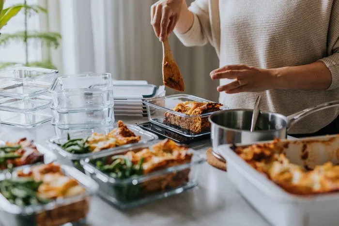 Person preparing meal prep containers with lasagna and green beans on a kitchen counter