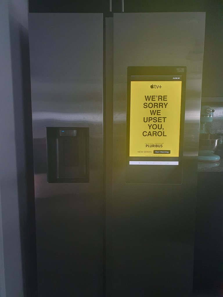A smart refrigerator displaying an Apple TV+ ad that reads "WE'RE SORRY WE UPSET YOU, CAROL."