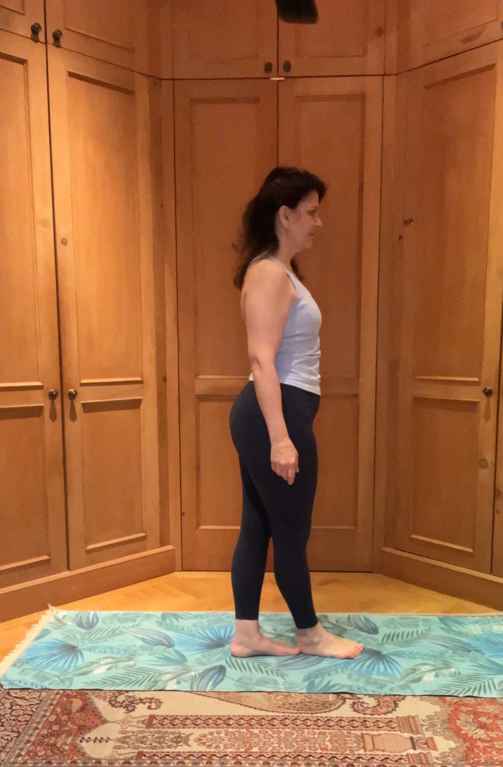person standing in profile on a yoga mat in a wooden room.