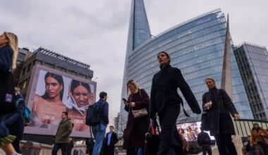 Commuters walk across London Bridge past a large ASOS advertisement, with The Shard and a modern glass office building in the background.