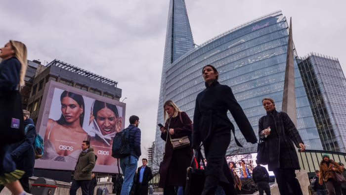 Commuters walk across London Bridge past a large ASOS advertisement, with The Shard and a modern glass office building in the background.