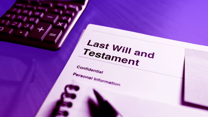 A document labelled "Last Will and Testament" on a desk next to a calculator and notepad.