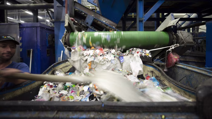 A worker moves a shovel while paper and plastic labels are processed on a conveyor at a recycling facility.