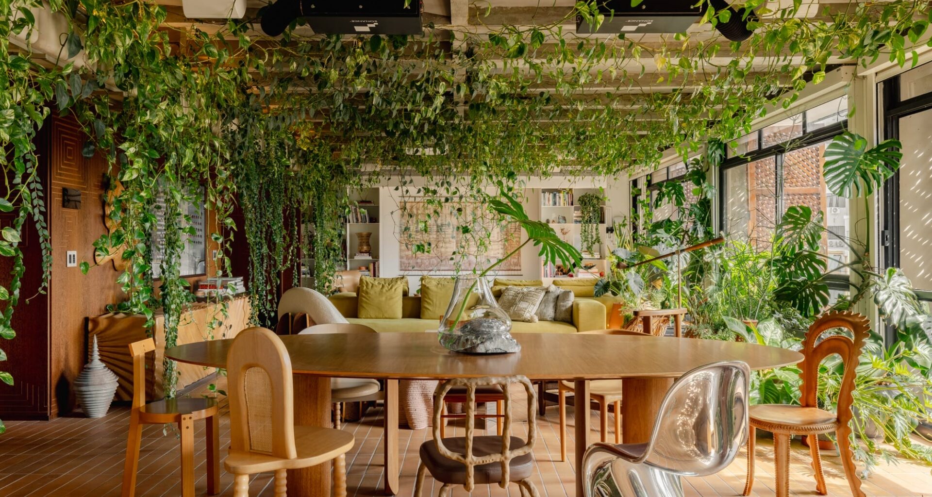 An apartment interior designed by Guto Requena with an eclectic variety of contemporary furnishings and houseplants draping from rafters in the ceiling