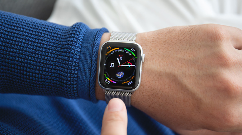 A closeup of an individual's wrist as they point to the Apple Watch on their wrist, the device is showing the Home screen.