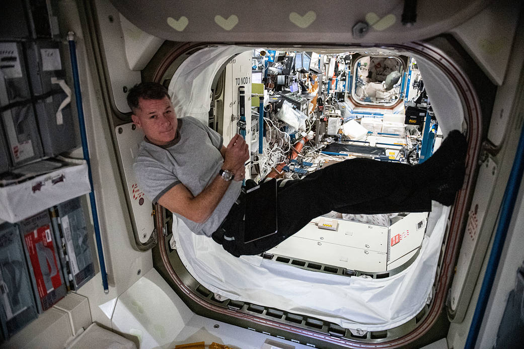 Astronaut Shane Kimbrough--a man with trim, dark hair, wearing a gray T-shirt and black pants--floats inside the vestibule connecting two modules of the International Space Station. 