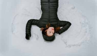 Woman in black winter coat making snow angels in snow.