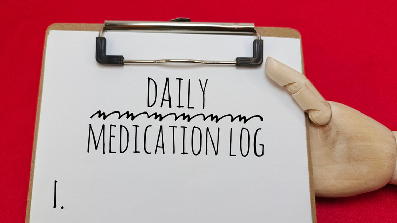 Mechanical hand holding daily medication log on clipboard.