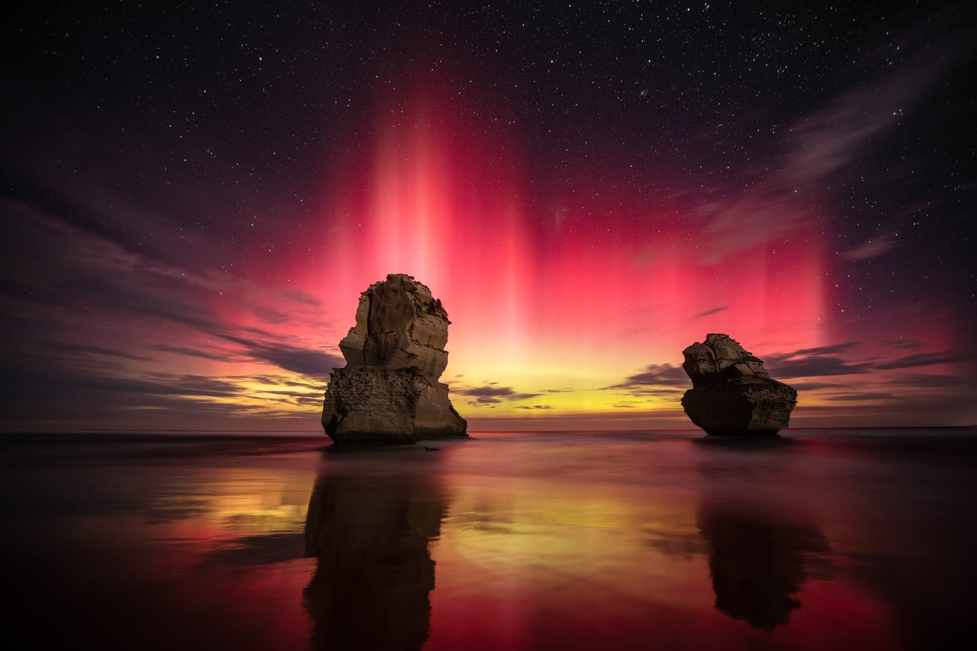 A colorful aurora borealis captured over a couple of sea stacks in the ocean