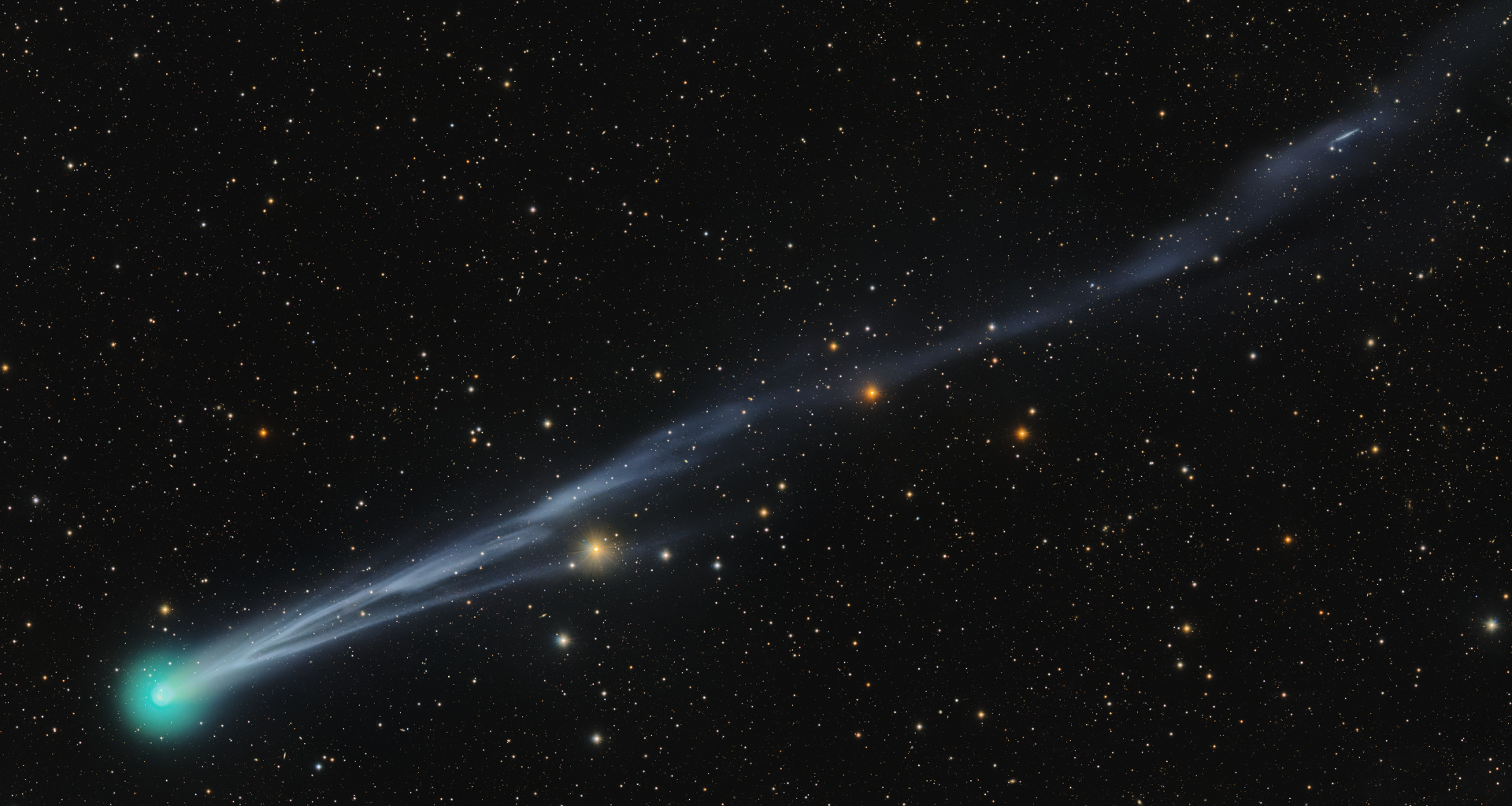 A bright green comet is pictured to the bottom left of a starfield against a black sky, with a long tail extending to the upper right of the screen.