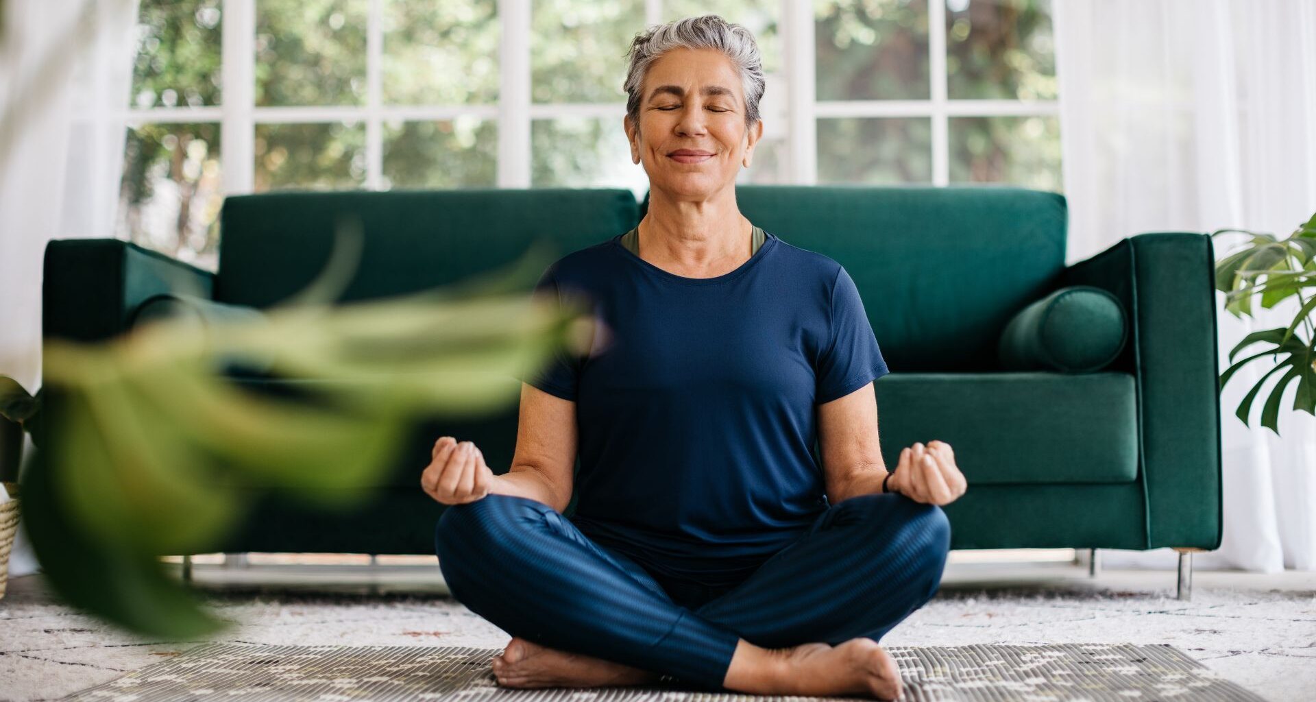 Woman sitting on rug in living room doing yoga over 60 poses, smiling