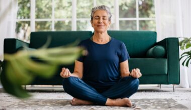 Woman sitting on rug in living room doing yoga over 60 poses, smiling