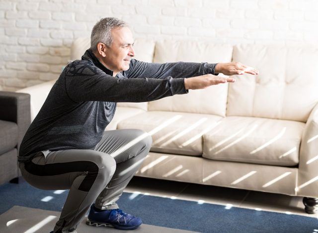 Senior man doing squats and exercising in living room at home