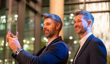 Two men, one holding a glass award trophy, stand next to each other smiling and looking to the left side of the photo.