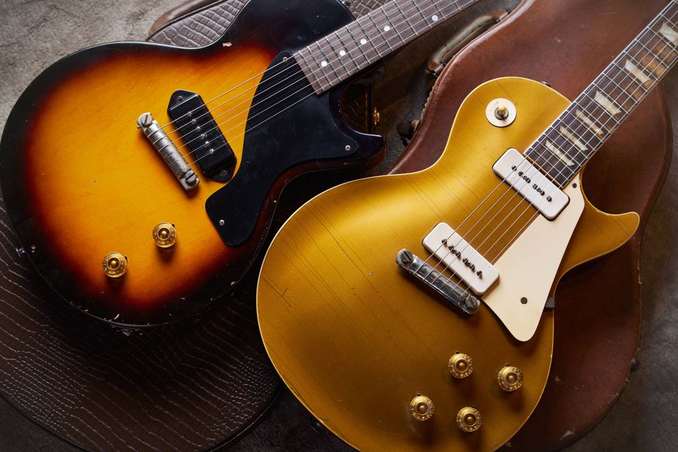 Two vintage electric guitars, one sunburst and one gold, resting on a textured surface.