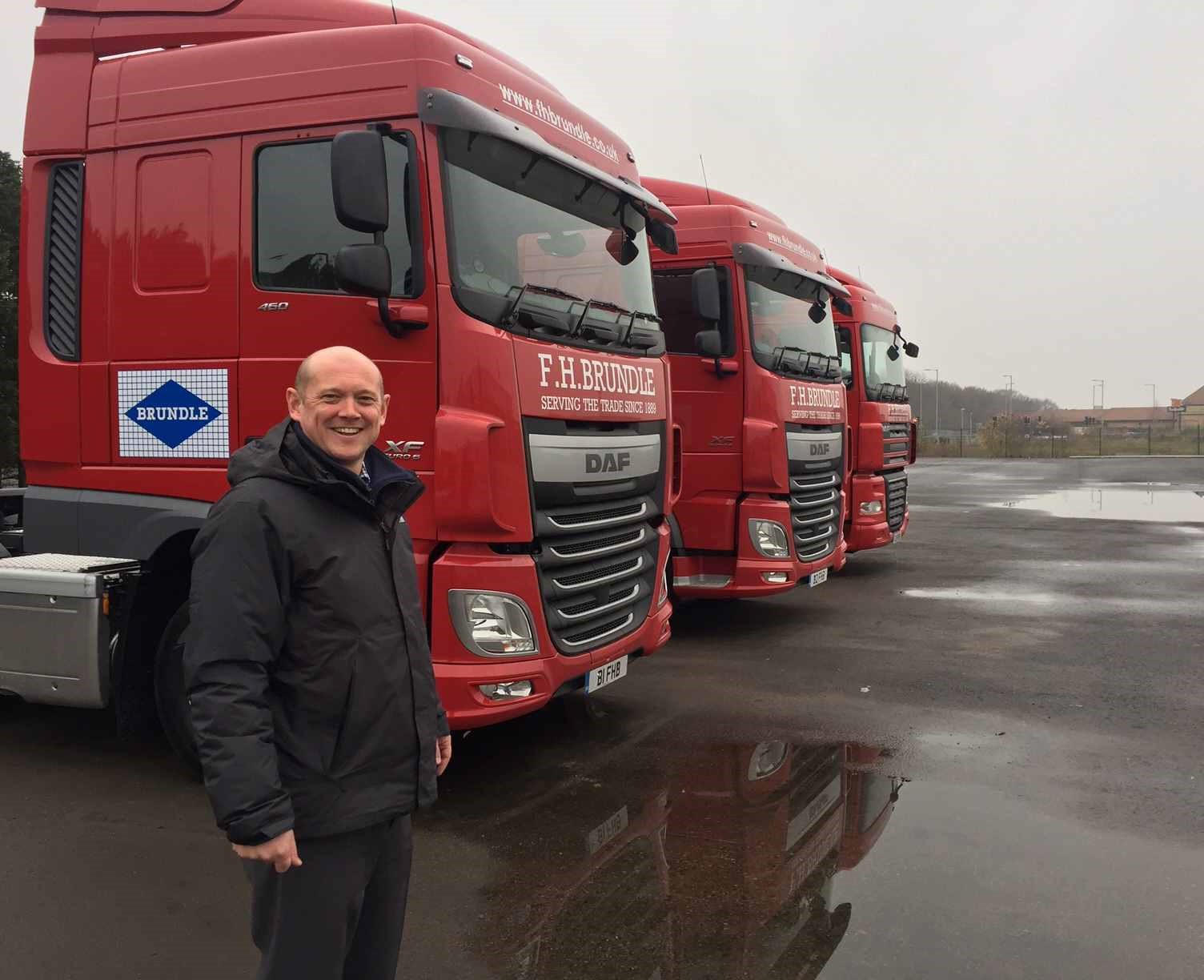 Michael Brundle, Director at F H Brundle, standing in front of three red F.H. Brundle trucks.