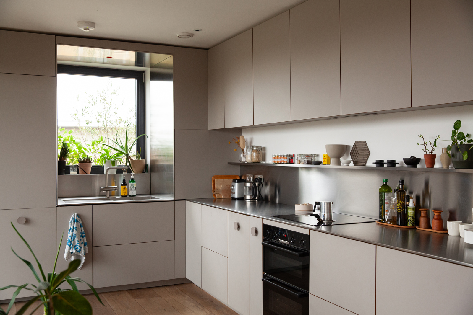 A modern kitchen with light gray cabinets, stainless steel countertops, and various plants and cooking items.