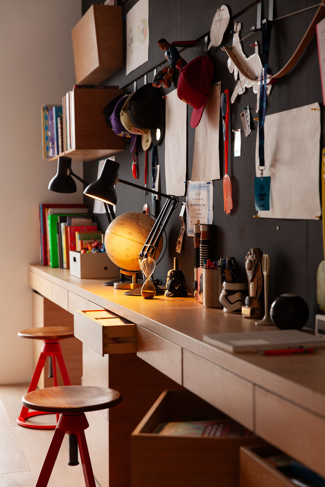 A child's study desk with two red stools, a globe, hourglass, and two lamps.