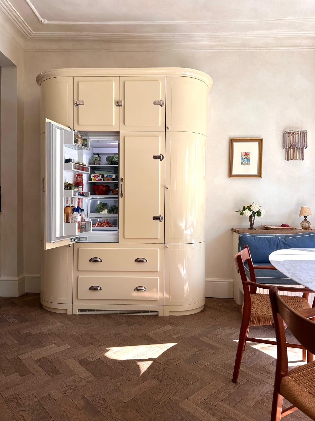 A concealed fridge by Matilda Goad with its door open, revealing organized food inside.