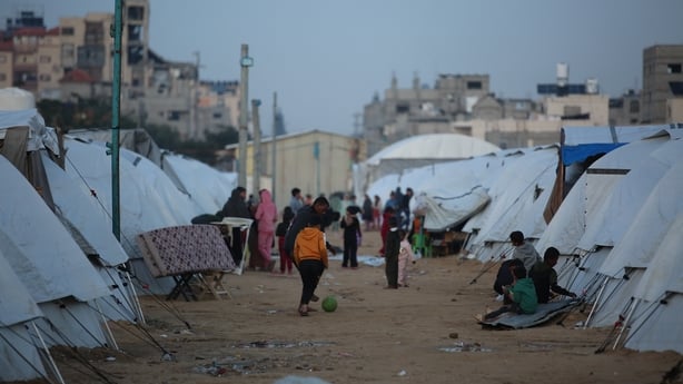 a boy is seen kicking a football on a dusty street with tents on either side
