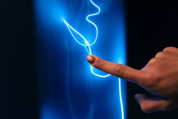 A close-up that captures a person's finger with glitter polish while touching a luminous surface. The contact generates an arc of blue light that winds over the dark background, symbolizing connection, energy, electricity, haptic technology. Ideal for themes of innovation, energy, artificial intelli
