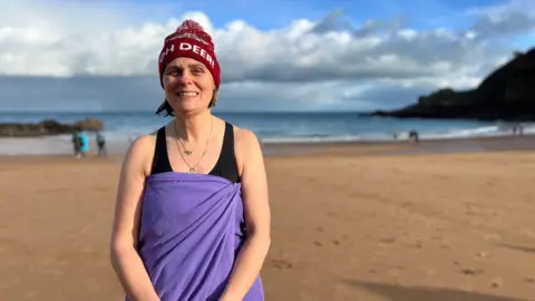 Woman wearing wooly hat and wrapped in towel on a beach 