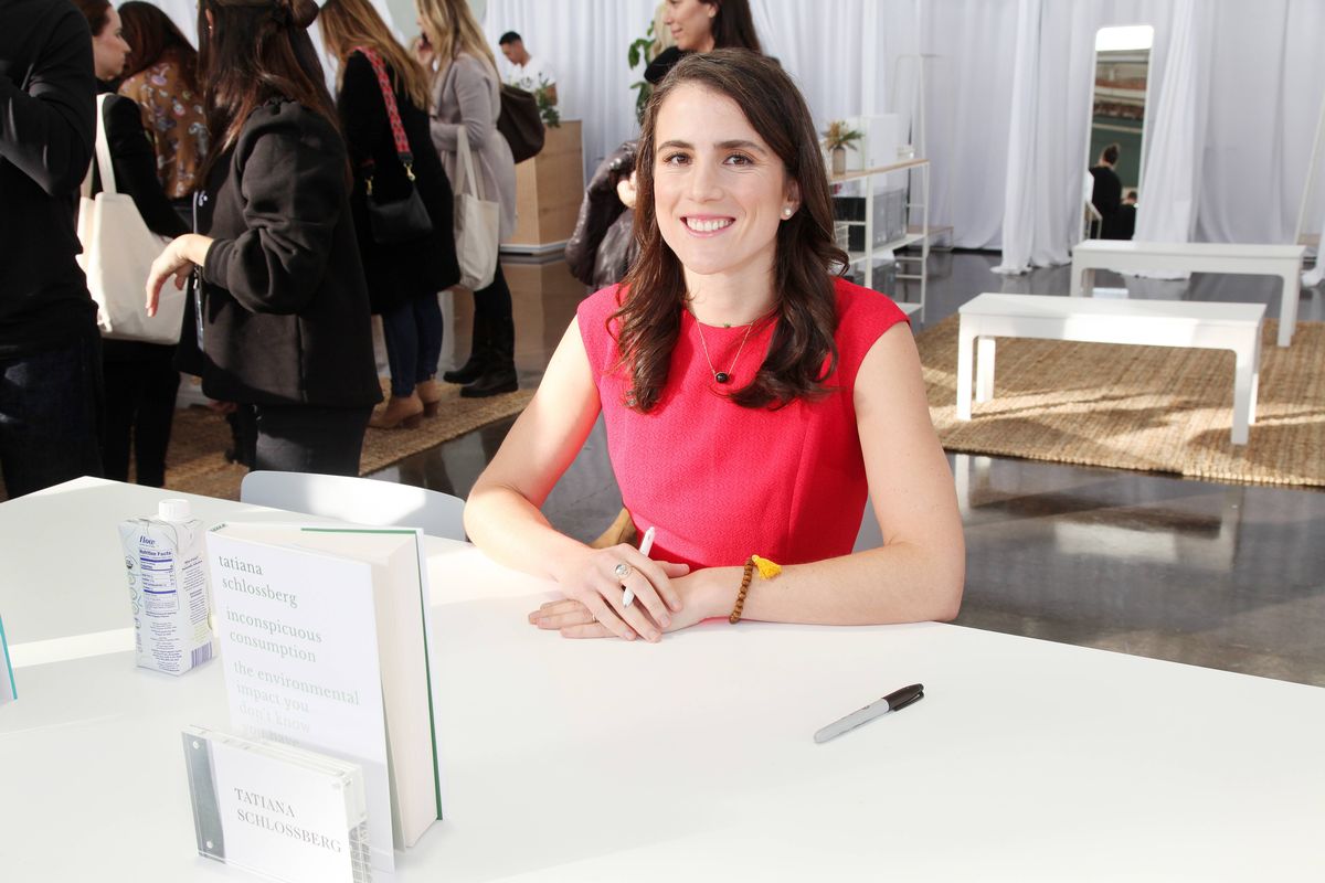 An individual with long, dark hair, dressed in a red top, is smiling brightly, perhaps in an indoor setting with blurred background elements including a white shelf and a wooden box.