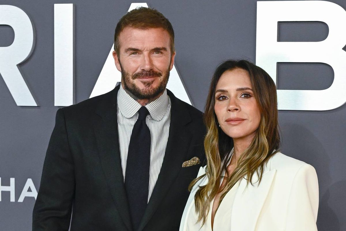 An individual in a formal suit and tie stands next to a woman in a white blazer, both positioned in front of a large, stylized sign featuring the letters "RIAB."