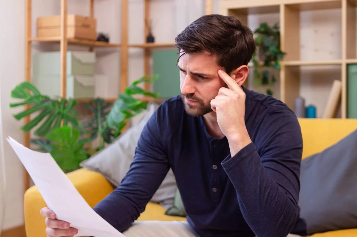 Stressed young man reading a letter and having a headache at home