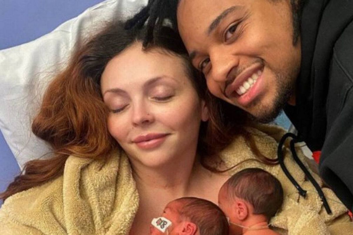 An adult individual reclining on a pillow, eyes closed, next to another adult individual who is smiling and looking at the camera.