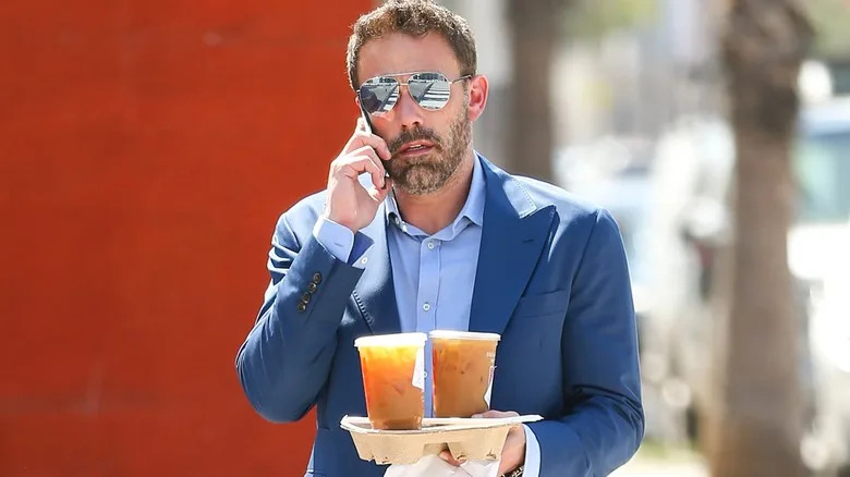 Ben Affleck talking on cellphone and holding a takeout tray with Dunkin' coffee
