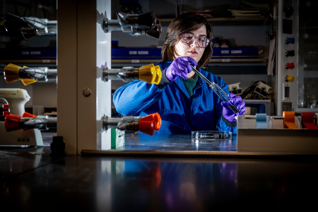 A person in lab coat and wearing gloves places recycled rubber into a test tube.