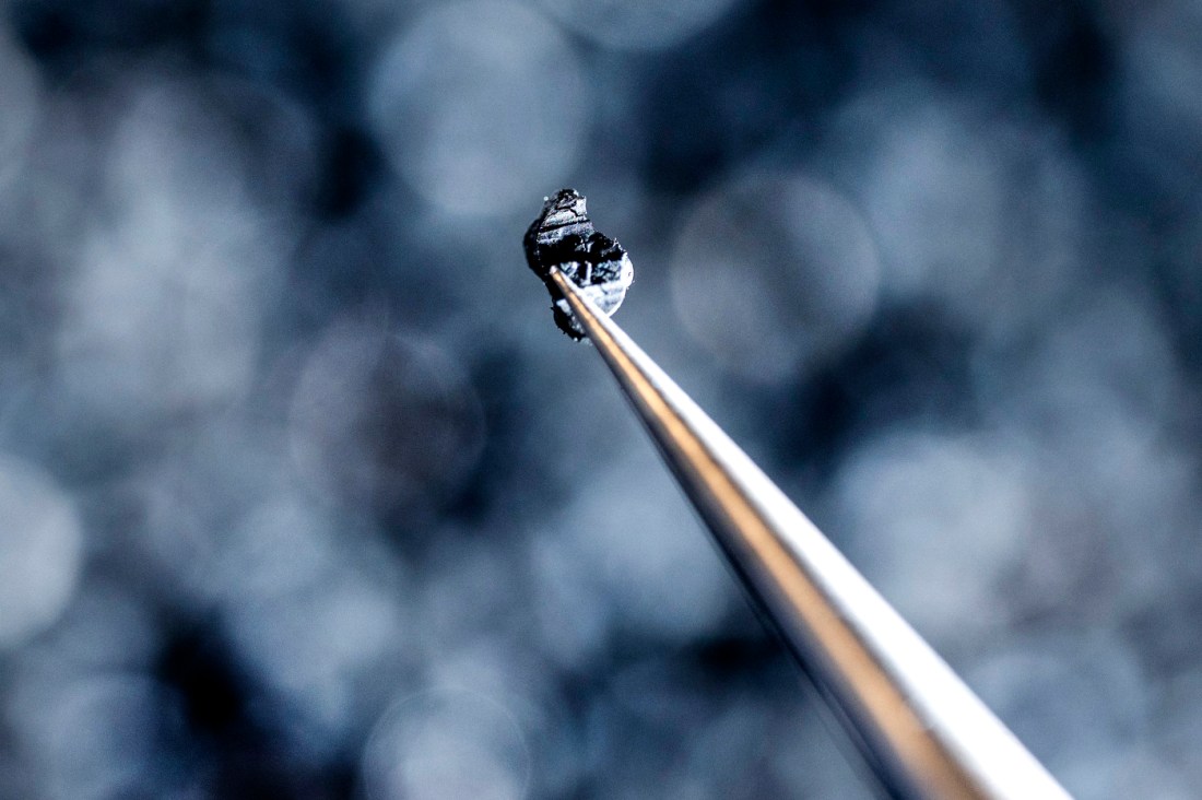 A macro photo of a pair of tweezers holding a single bead of crumb rubber.