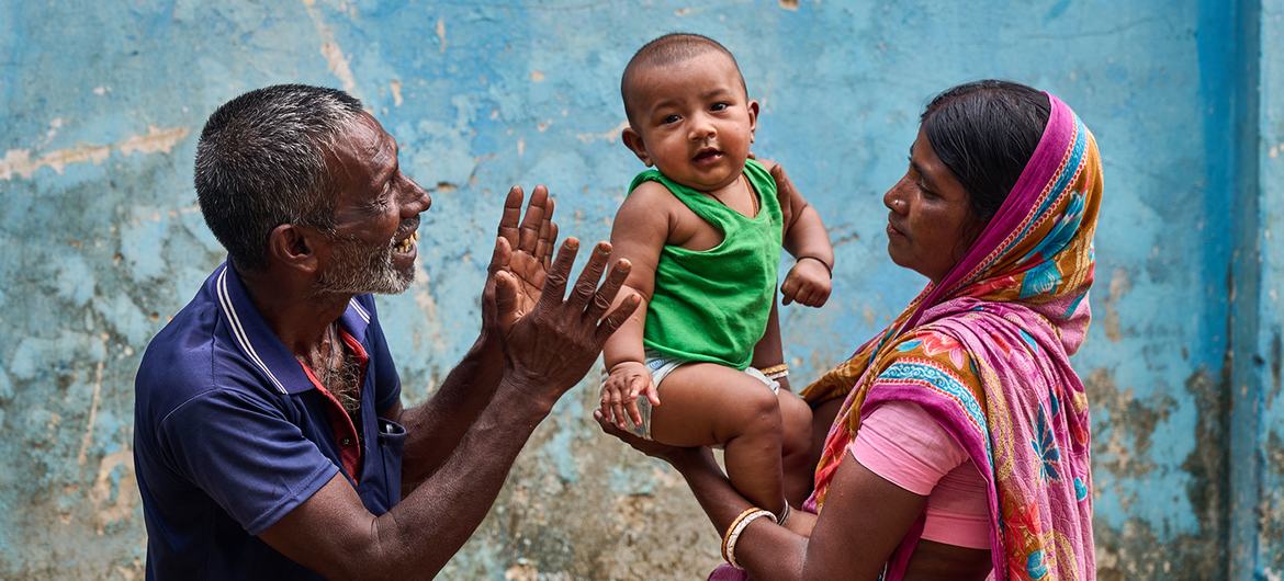 A baby is held by his mother and entertained by his grandfather at a community clinic in northern Bangladesh.