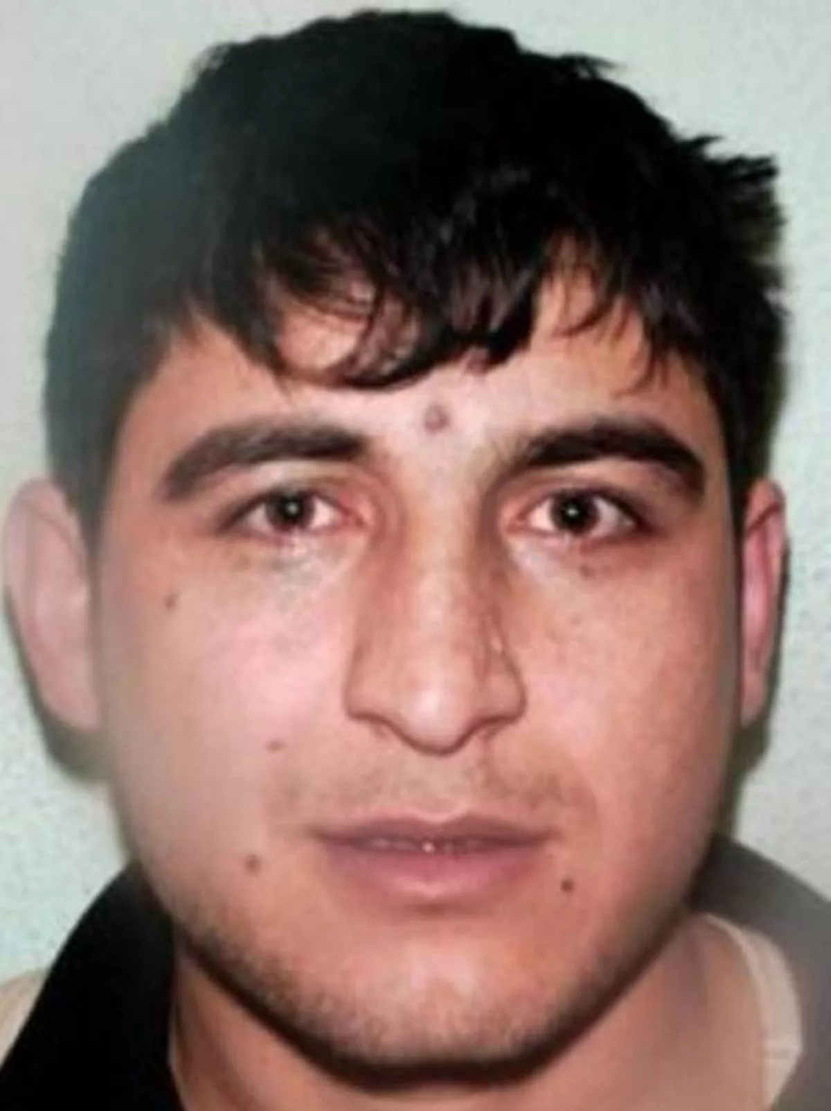 A close-up image of an individual's face, featuring distinct facial features such as a prominent nose, brown eyes, and a slight blemish on the forehead. The person's expression appears neutral, and their hair is styled in a manner typical for the region.