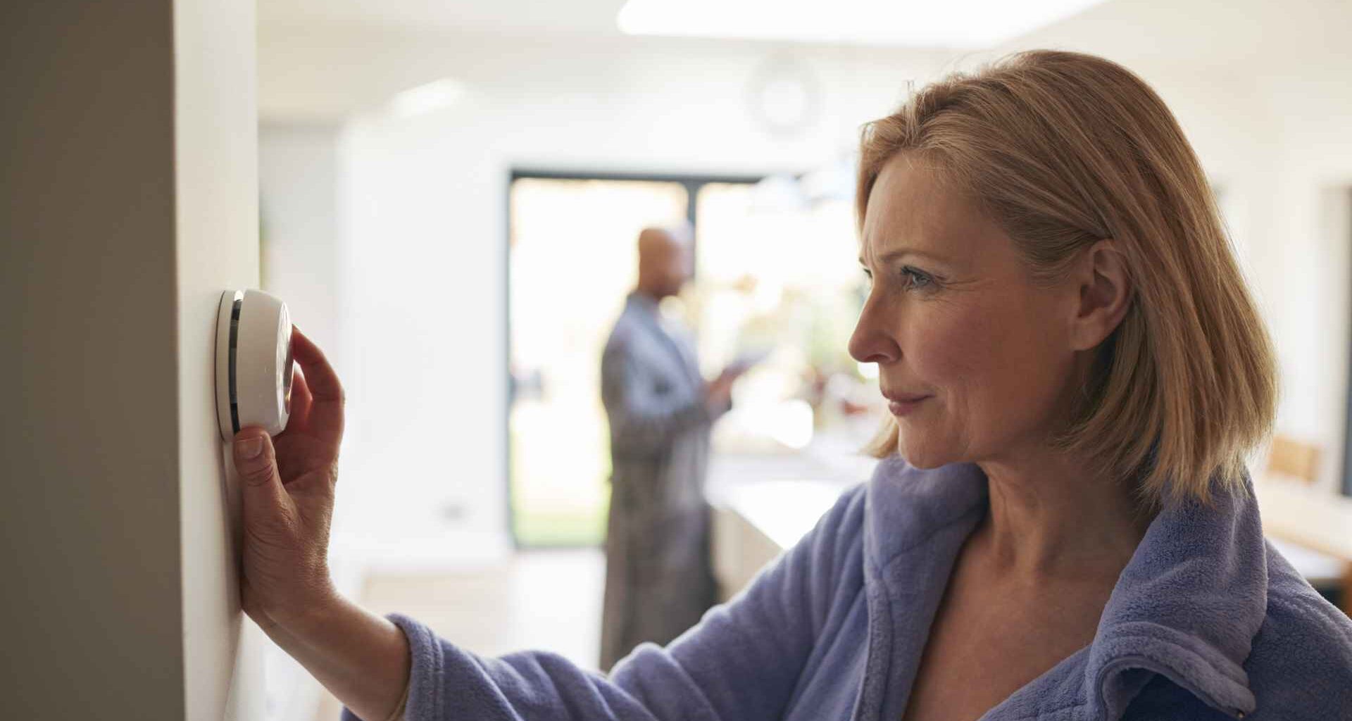 Mature Woman Turning Control Dial On Digital Central Heating Thermostat At Home.