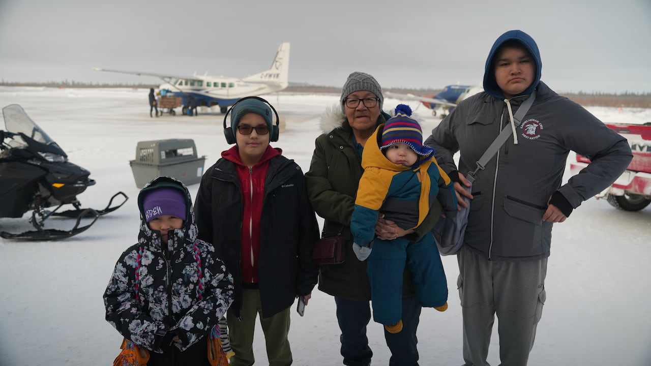 And older woman and four children standing outside at an airport.