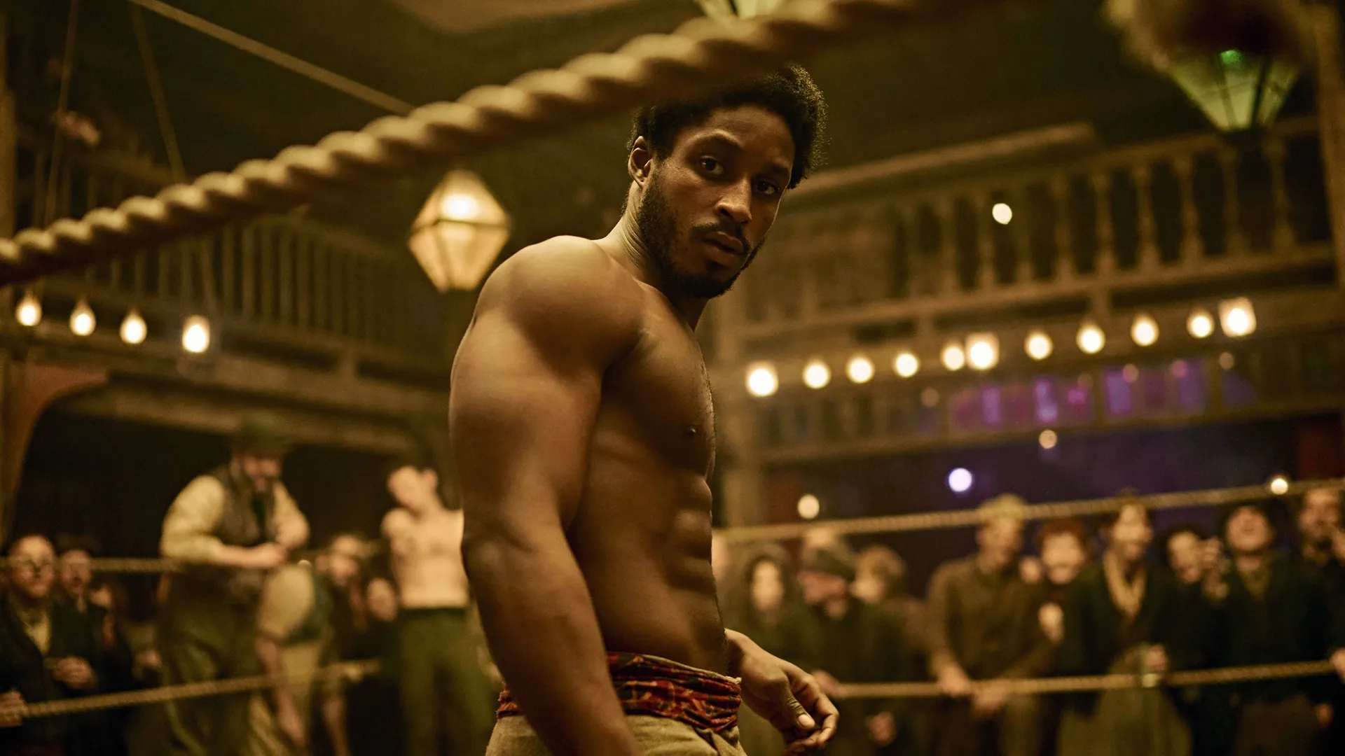 Alec Munroe (Francis Lovehall) stands in a boxing ring looking out towards the crowd