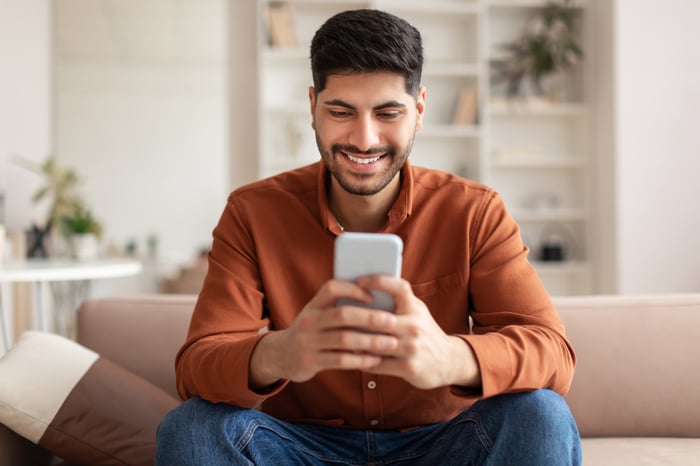 An investor smiles while looking at something on a smartphone.